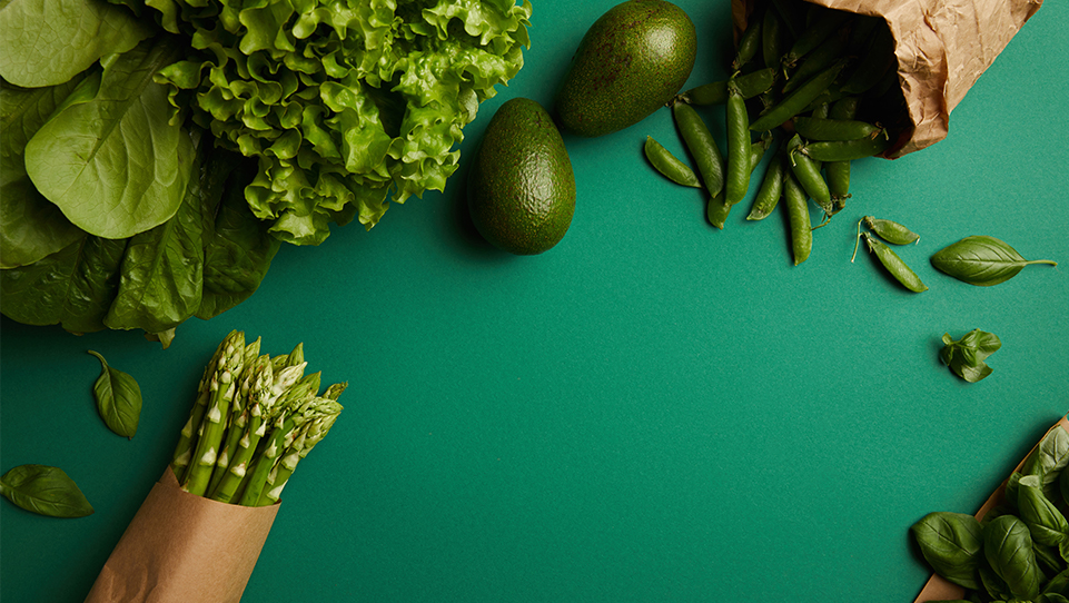 Zielone warzywa i owoce: awokado, szparagi, groszek, szpinak i sałata na zielonym materiale.