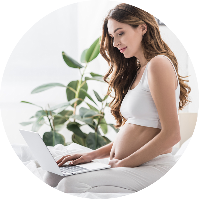 Uśmiechnięta kobieta w ciąży siedzi na kanapie z laptopem na kolanach