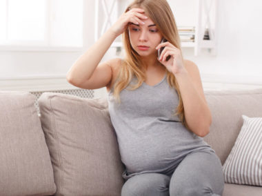 Zmartwiona kobieta w ciąży rozmawia przez telefon na kanapie