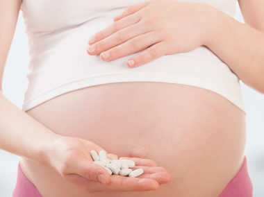 Kobieta w ciąży trzyma w dłoni tabletki