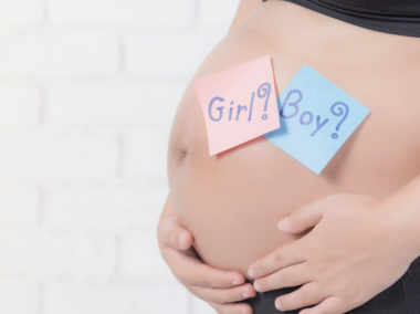 Brzuch kobiety w ciąży. Na jej brzuchu znajdują się dwie karteczki, na jednej widnieje napis "Girl?, na drugiej "Boy?".