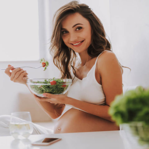 Uśmiechnięta kobieta w ciąży je sałatkę