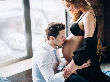 Młoda para. Mężczyzna siedzi i całuję w brzuch kobietę, która jest w ciąży.