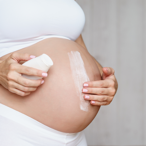 Kobieta w ciąży smaruje kremem skórę na brzuchu.